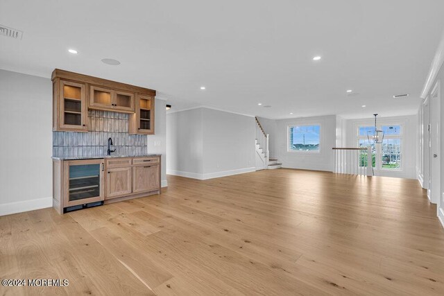 unfurnished living room with wine cooler, wet bar, crown molding, and light hardwood / wood-style floors