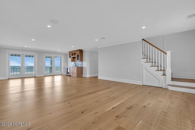 unfurnished living room with ornamental molding, light wood-type flooring, and french doors