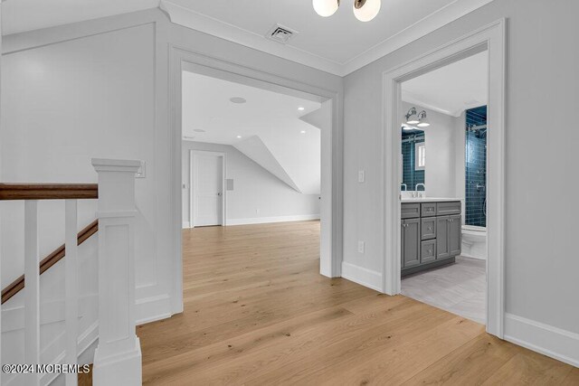 corridor with light wood-type flooring, crown molding, and sink