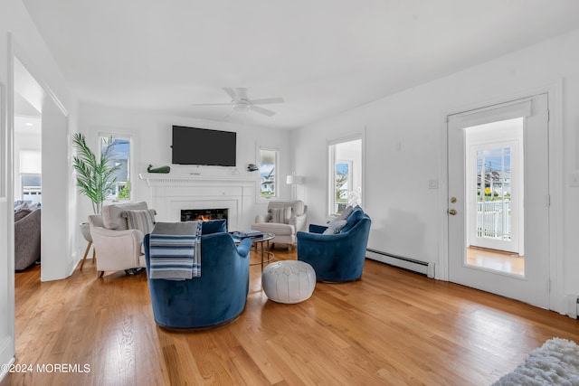 living room with a baseboard heating unit, ceiling fan, a wealth of natural light, and light hardwood / wood-style floors