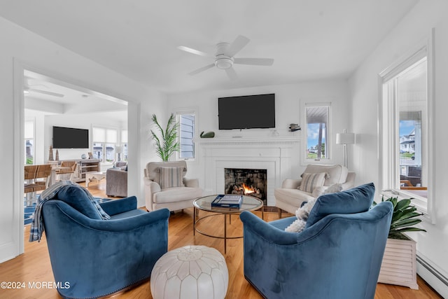 living room featuring a baseboard heating unit, ceiling fan, a fireplace, and light hardwood / wood-style floors