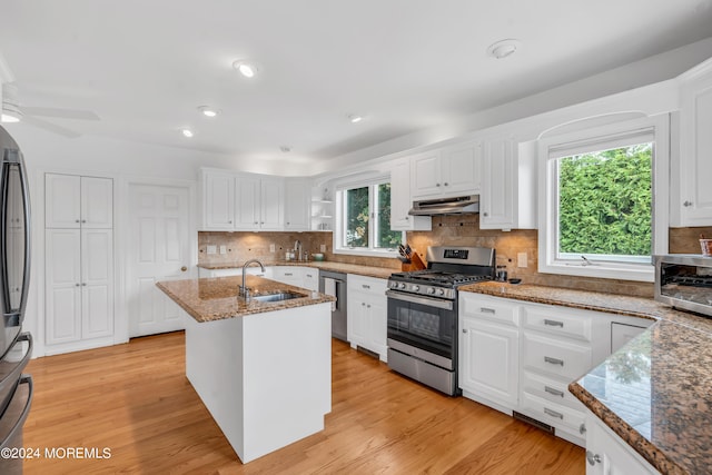 kitchen featuring stone countertops, light hardwood / wood-style flooring, sink, appliances with stainless steel finishes, and a center island with sink