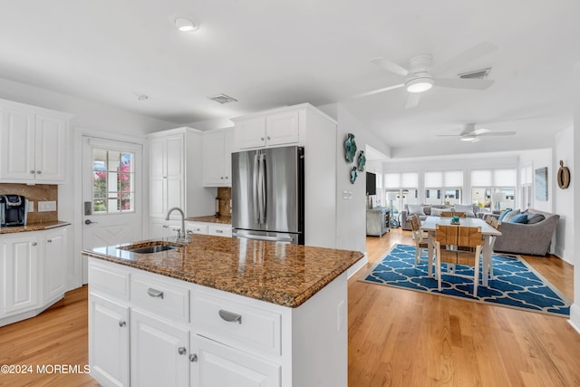 kitchen with stainless steel refrigerator, sink, dark stone counters, ceiling fan, and a kitchen island with sink