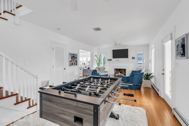 recreation room featuring light wood-type flooring, a baseboard radiator, and ceiling fan