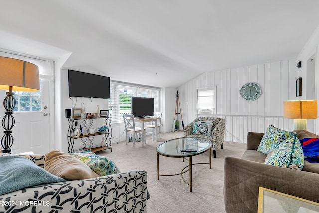 living room featuring lofted ceiling, wood walls, a wealth of natural light, and light carpet