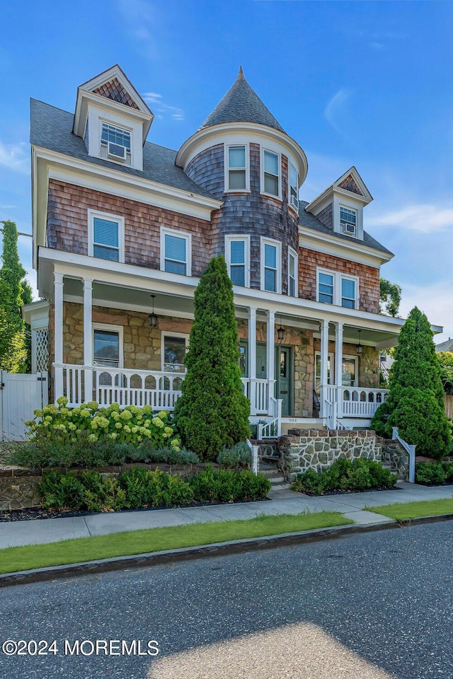 shingle-style home featuring a porch, fence, stone siding, and a shingled roof