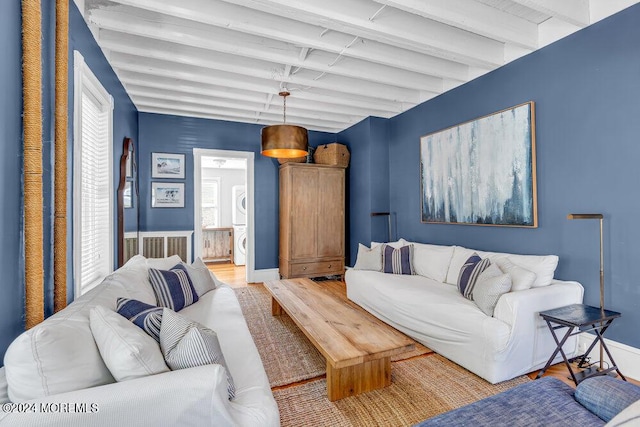 living room with beamed ceiling, light wood-style floors, baseboards, and stacked washing maching and dryer