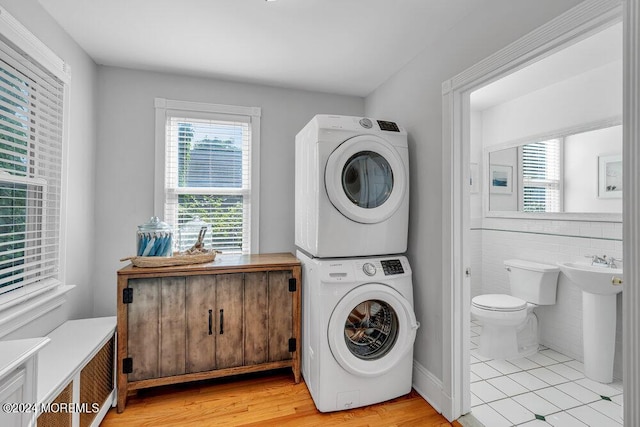 laundry room featuring laundry area, stacked washer and clothes dryer, tile walls, and light wood-style floors