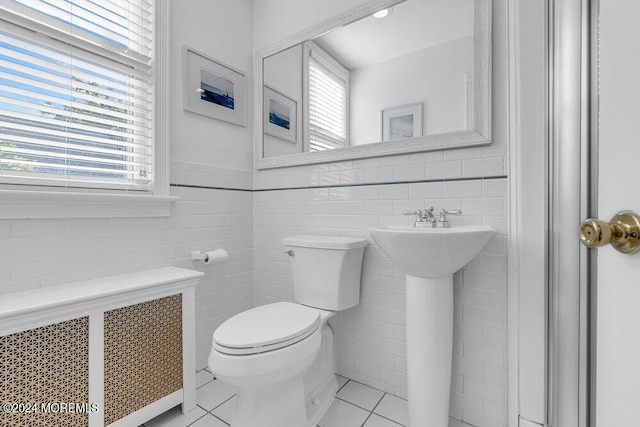 half bathroom with radiator, a sink, tile patterned floors, toilet, and tile walls