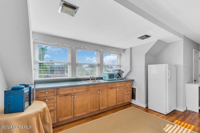 kitchen featuring visible vents, light wood-style flooring, freestanding refrigerator, a sink, and brown cabinets