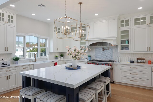 kitchen with designer range, white cabinetry, a kitchen island, light stone countertops, and decorative backsplash