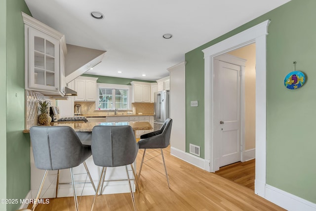 kitchen featuring white cabinetry, high end refrigerator, light hardwood / wood-style flooring, stove, and decorative backsplash