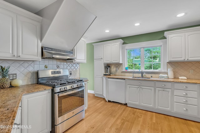 kitchen with white cabinets, wall chimney range hood, sink, appliances with stainless steel finishes, and light hardwood / wood-style floors