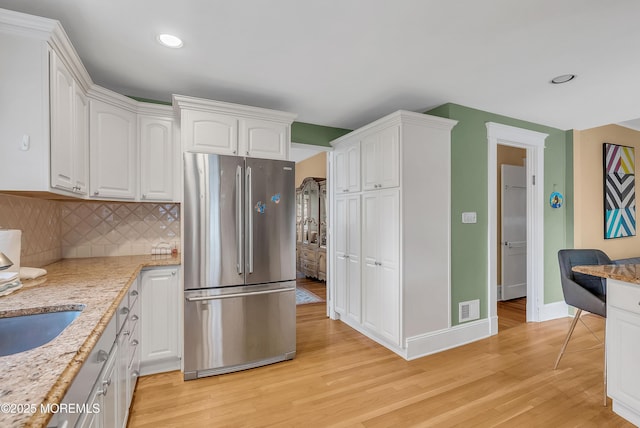 kitchen with tasteful backsplash, light stone counters, white cabinets, light hardwood / wood-style floors, and stainless steel refrigerator