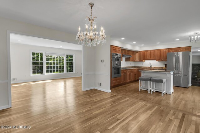 kitchen featuring light hardwood / wood-style flooring, an inviting chandelier, an island with sink, appliances with stainless steel finishes, and a breakfast bar area