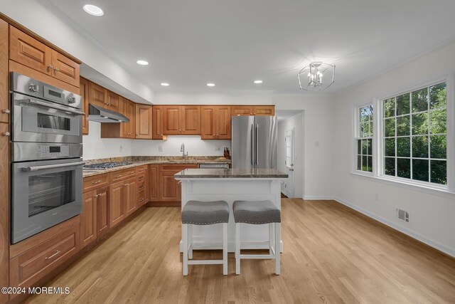 kitchen featuring light wood-type flooring, stainless steel appliances, a chandelier, a kitchen breakfast bar, and a kitchen island