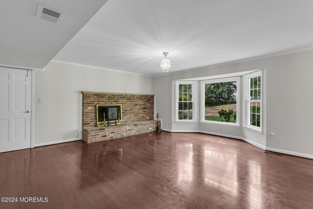 unfurnished living room with crown molding, an inviting chandelier, dark hardwood / wood-style flooring, and a fireplace