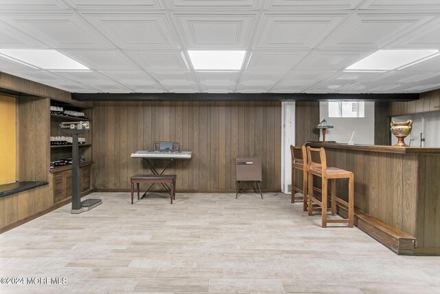 basement with bar area, wood walls, and light hardwood / wood-style flooring