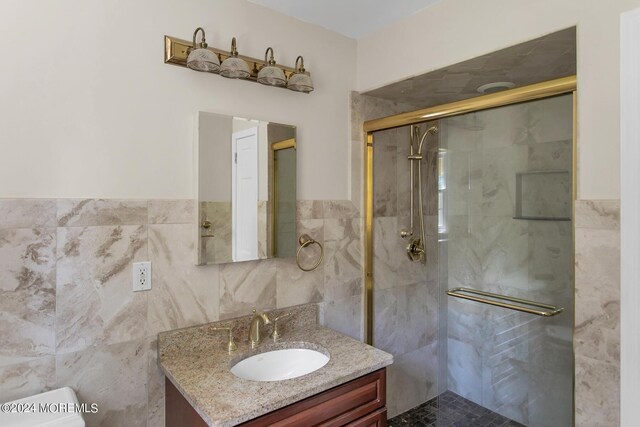 bathroom with a shower with door, vanity, toilet, and tile walls