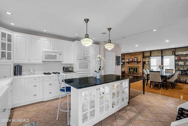 kitchen with light tile patterned floors, white appliances, a brick fireplace, and glass insert cabinets