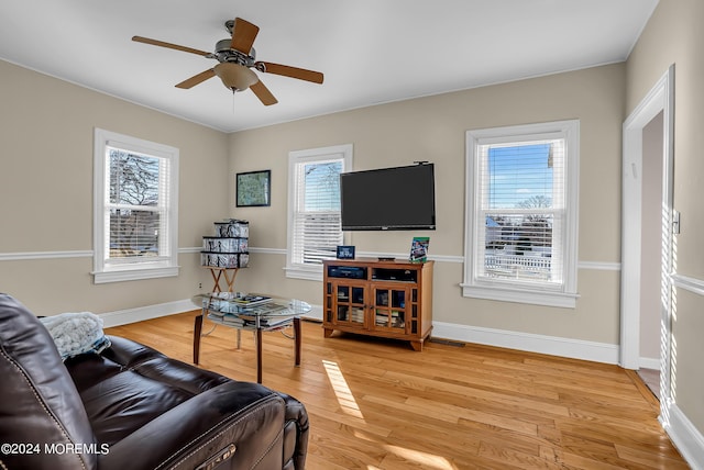 living area with light wood-type flooring, ceiling fan, visible vents, and baseboards