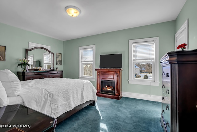 bedroom with carpet floors, a glass covered fireplace, multiple windows, and baseboards