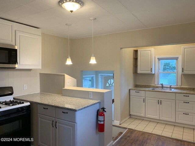 kitchen featuring stainless steel microwave, a peninsula, gas stove, white cabinetry, and a sink