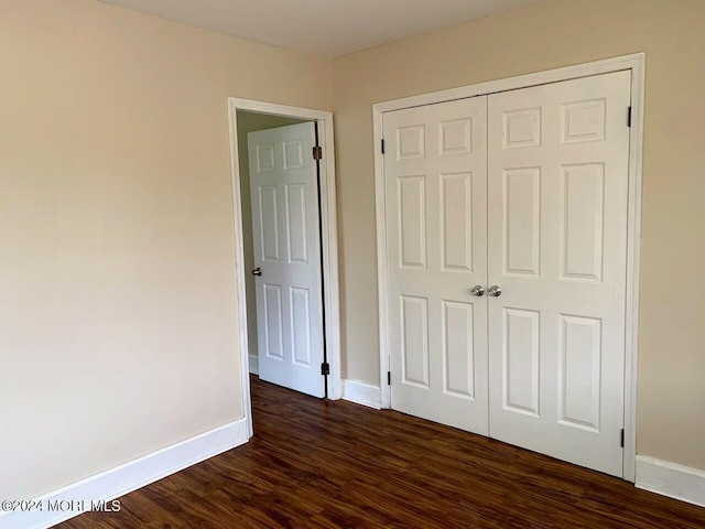 unfurnished bedroom featuring baseboards, dark wood-style flooring, and a closet