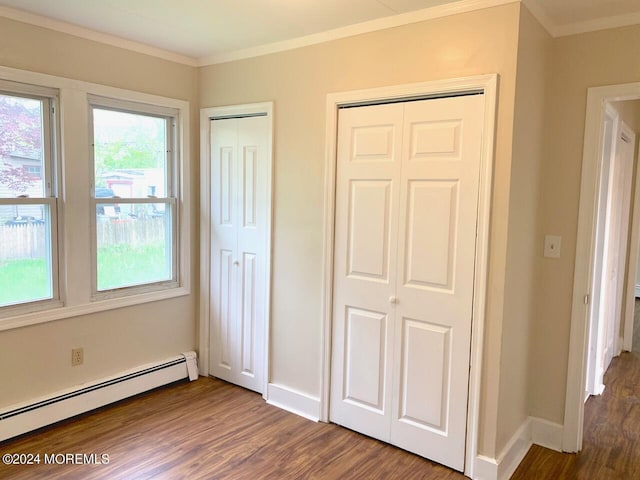 unfurnished bedroom with dark wood-type flooring, baseboards, multiple closets, ornamental molding, and baseboard heating