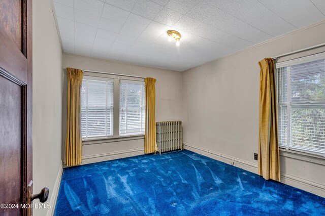 empty room featuring ornamental molding, dark carpet, and radiator heating unit