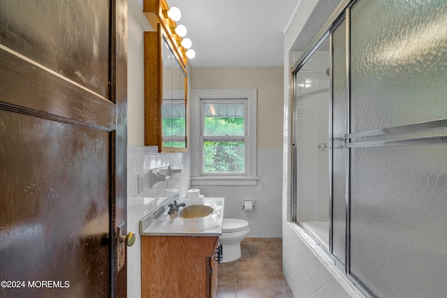 full bathroom featuring vanity, toilet, combined bath / shower with glass door, tile walls, and tile patterned flooring