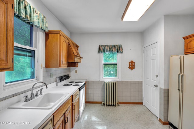 kitchen with radiator heating unit, a wealth of natural light, white appliances, and sink