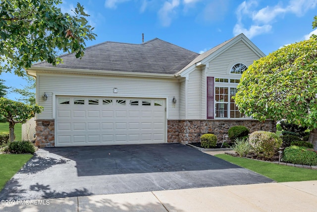 view of front facade with stone siding, a shingled roof, an attached garage, and driveway