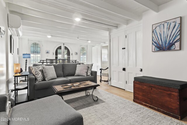 living room with a wealth of natural light, light hardwood / wood-style flooring, beam ceiling, and a wall mounted air conditioner