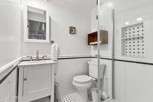 bathroom featuring vanity, toilet, walk in shower, and tile walls