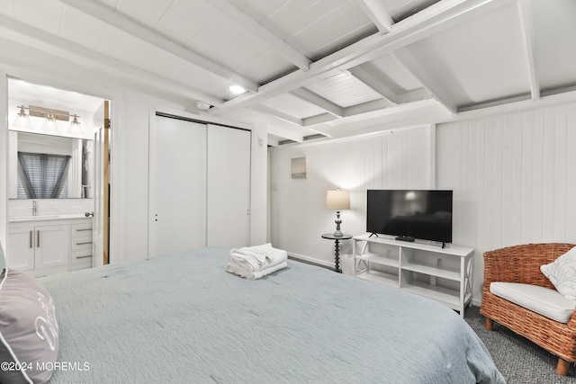 bedroom with a closet, ensuite bath, beamed ceiling, and a sink