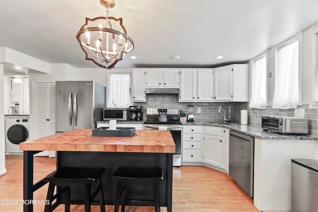 kitchen featuring white cabinets, stainless steel appliances, a notable chandelier, wooden counters, and washer / dryer