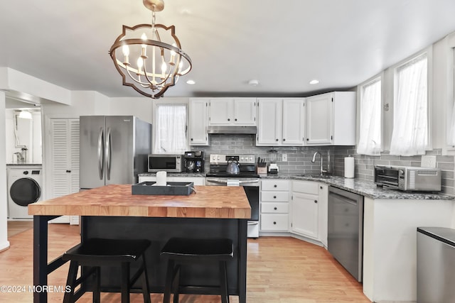 kitchen with washer / dryer, butcher block counters, stainless steel appliances, under cabinet range hood, and a sink