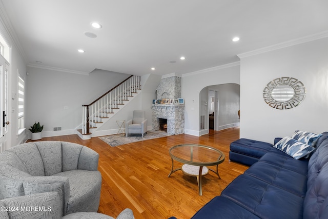 living room featuring a stone fireplace, crown molding, and wood-type flooring