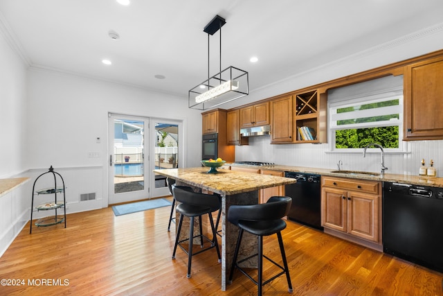 kitchen featuring light stone countertops, black appliances, decorative light fixtures, a breakfast bar, and sink