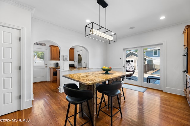 kitchen with light stone countertops, crown molding, a breakfast bar, and kitchen peninsula