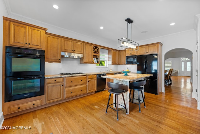 kitchen with light stone counters, black appliances, a breakfast bar, a center island, and ornamental molding