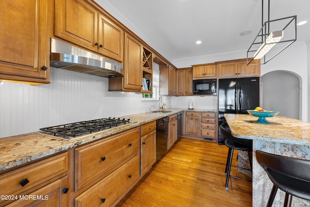 kitchen featuring decorative light fixtures, black appliances, light hardwood / wood-style floors, sink, and light stone counters