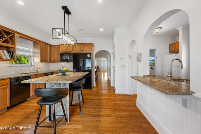 kitchen with sink, light stone counters, a kitchen island, black appliances, and a breakfast bar area