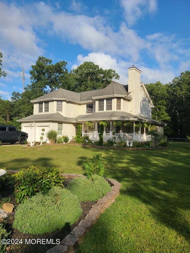 rear view of property with covered porch, a yard, and a garage