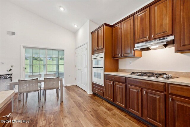 kitchen featuring stainless steel gas cooktop, light hardwood / wood-style floors, white double oven, and vaulted ceiling