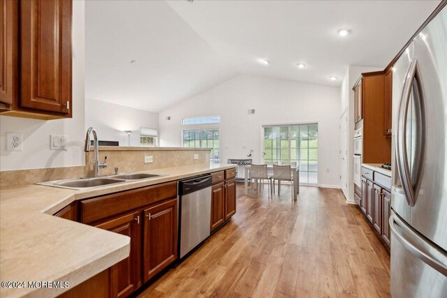 kitchen featuring appliances with stainless steel finishes, lofted ceiling, sink, and light hardwood / wood-style floors