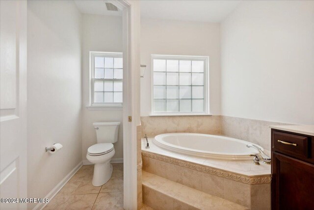 bathroom with tiled tub, toilet, vanity, and tile patterned floors