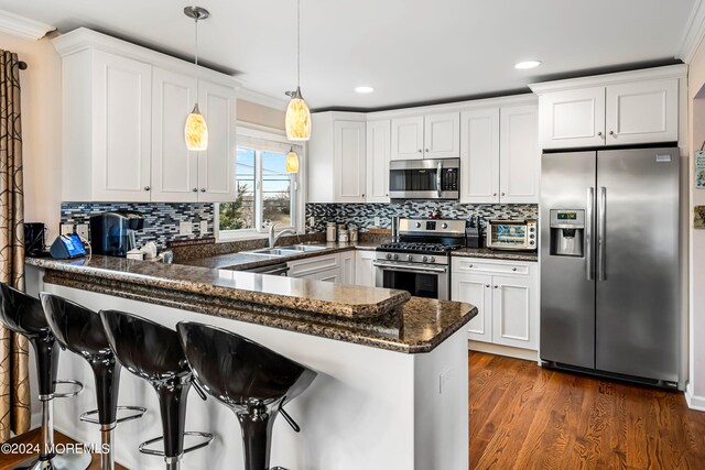 kitchen featuring dark wood finished floors, a peninsula, a sink, white cabinets, and appliances with stainless steel finishes