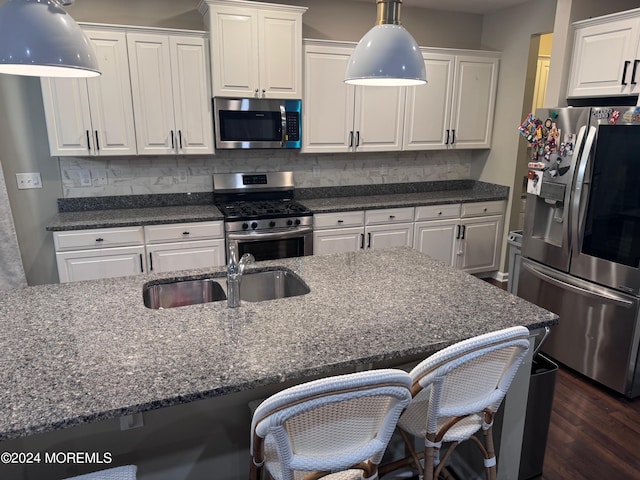 kitchen with a breakfast bar area, white cabinetry, stainless steel appliances, dark hardwood / wood-style flooring, and dark stone countertops